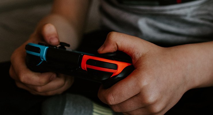 Kids, Quarantine & Devices: Managing Screen Time During COVID and Beyond by Joshua Wayne. photograph of a child holding a video game controller by Kelly Sikkema.